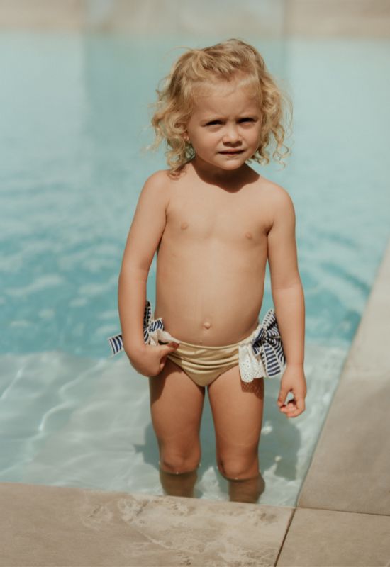 Culetín de baño dorado con volante de puntilla blanca y lazos marino en laterales para niña.